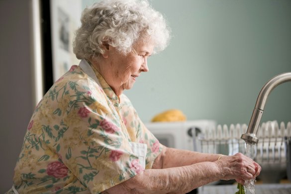 Elderly resident washing vegetables under kitchen sink tap