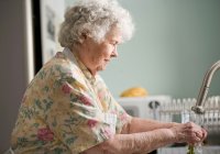 Elderly resident washing vegetables under kitchen sink tap