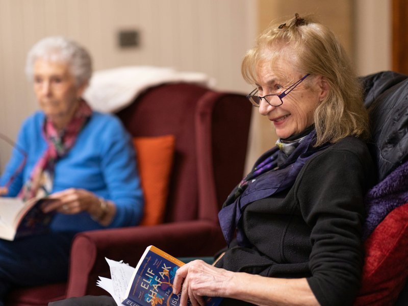 Female resident holding a book and smiling in a welcoming communal area